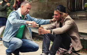 A man giving a homeless man a drink.